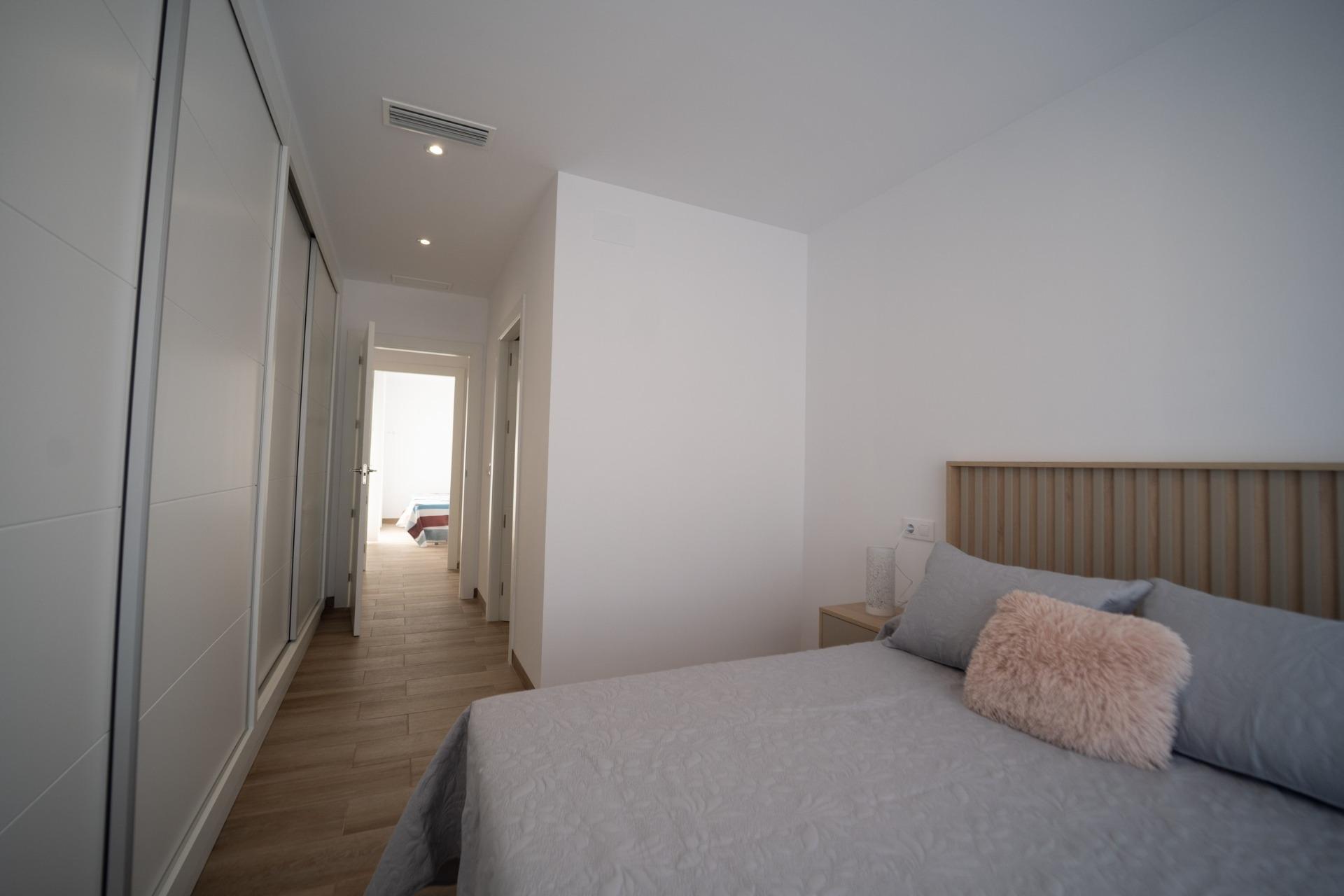 NEW-BUILD-TOWNHOUSES-IN-SAN-JAVIER-19 Bright modern bedroom with sleek built-in wardrobes and cozy wooden headboard in new build townhouses in San Javier.