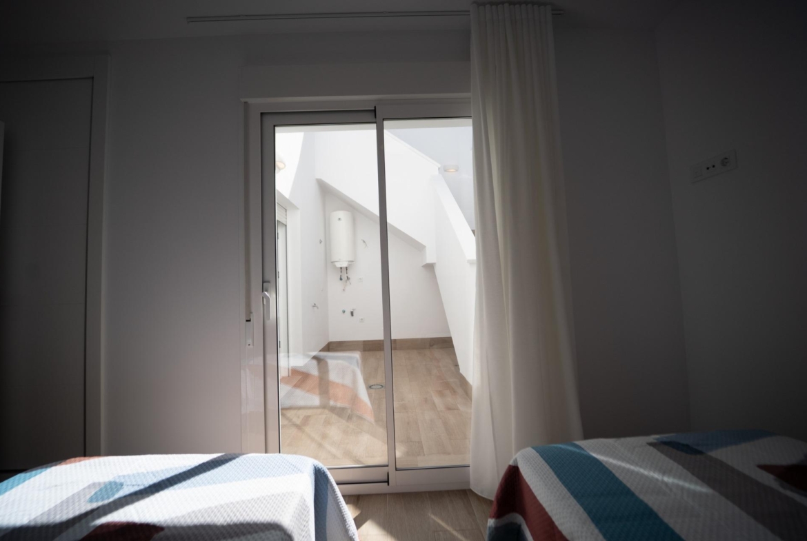 Bright twin bedroom with sliding glass doors opening to a private sunlit terrace in modern new build townhouses in San Javier.