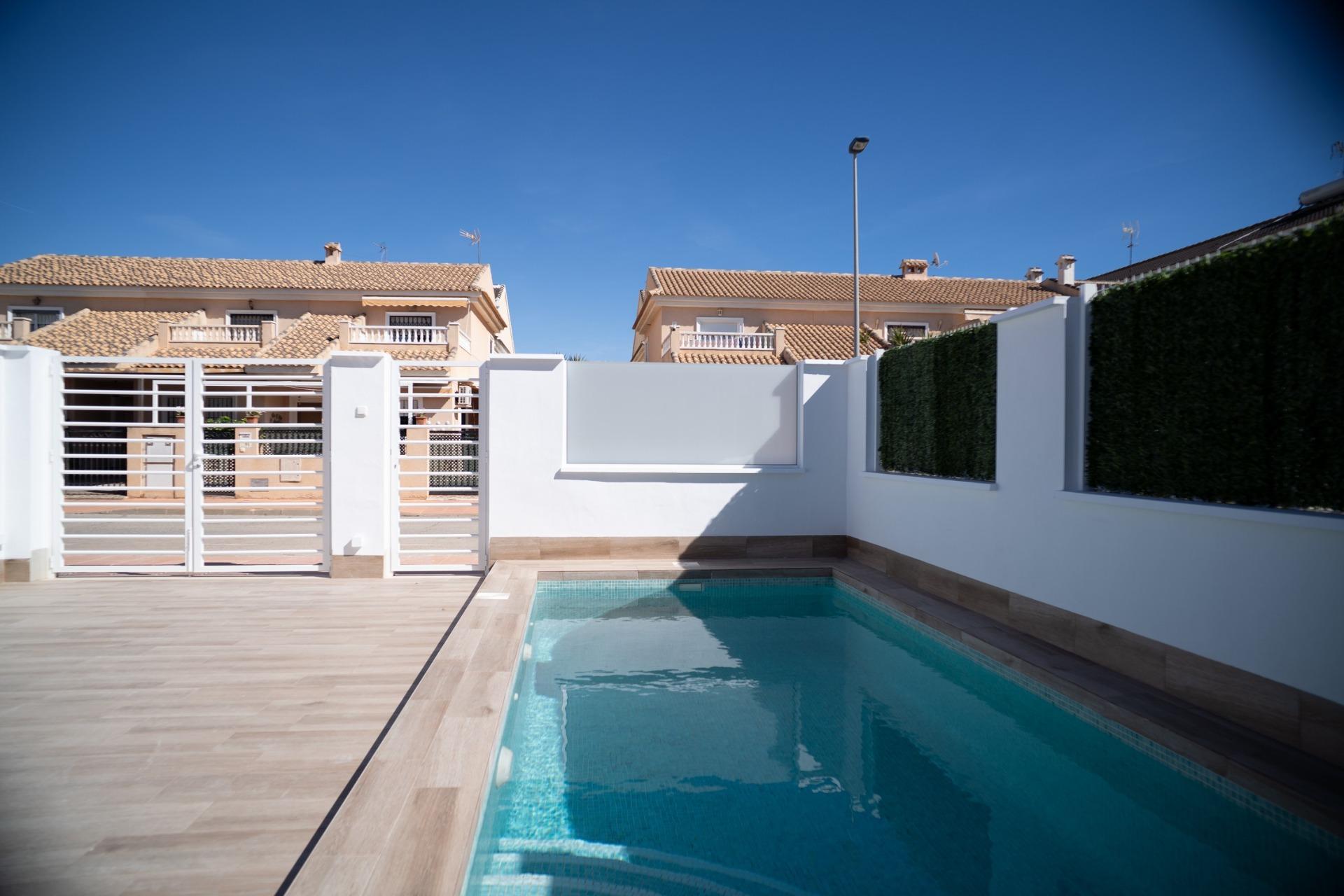 NEW-BUILD-TOWNHOUSES-IN-SAN-JAVIER-3 Private sunlit pool with sleek tiled terrace and modern gated façade of new build townhouses in San Javier