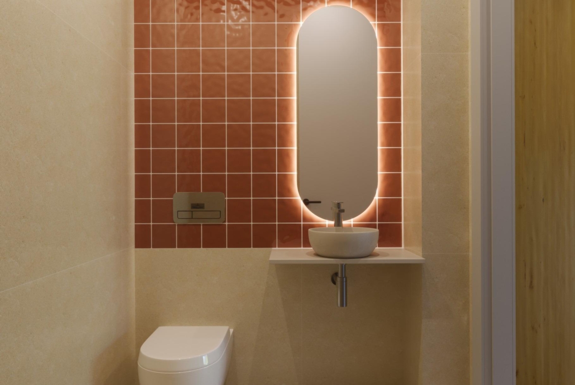 Modern guest bathroom with warm terracotta tiles and illuminated oval mirror in luxury 3-bedroom villa, Sierra Cortina Finestrat