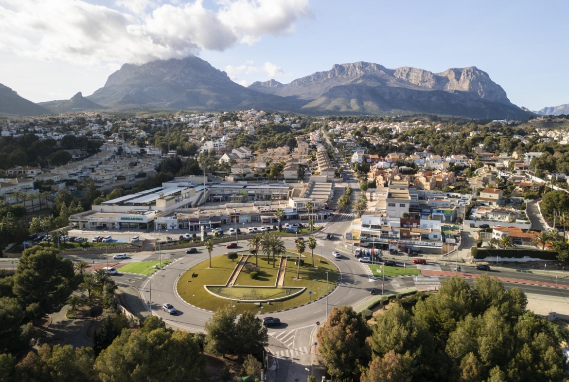 Aerial view of sunlit La Nucia town with lush greenery and mountain backdrop near the modern new build 3 bedroom villa in Costa Blanca.