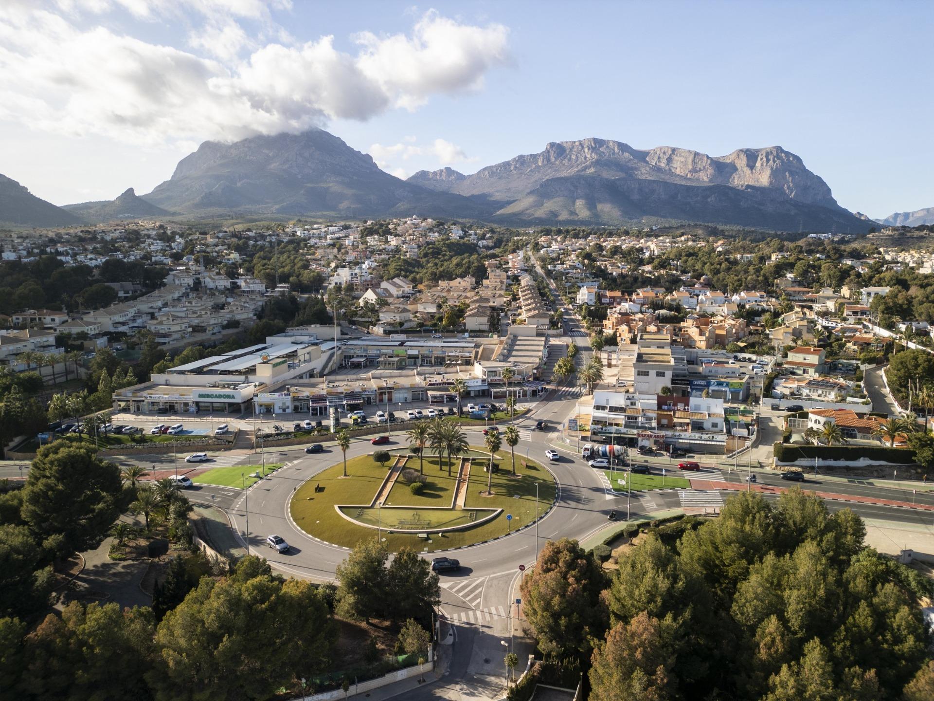 Aerial view of sunlit La Nucia town with lush greenery and mountain backdrop near the modern new build 3 bedroom villa in Costa Blanca.