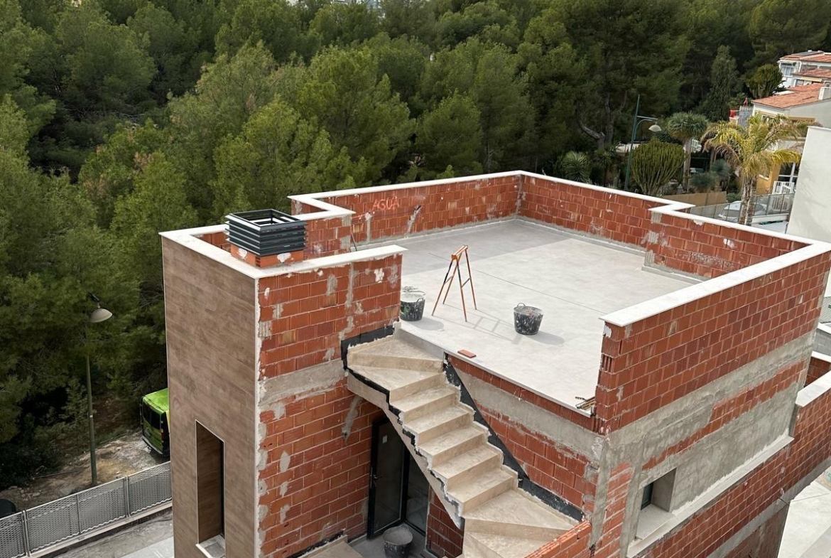 Unfinished modern 3-bedroom villa under construction with rooftop terrace in La Nucia, Costa Blanca, surrounded by lush greenery.