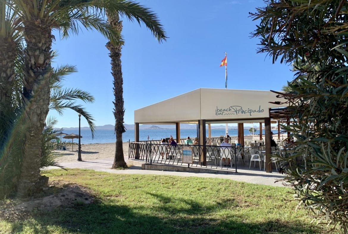 Sunlit beachfront terrace with palm trees overlooking the pristine beach near luxury new build villas in Los Alcázares, Murcia.