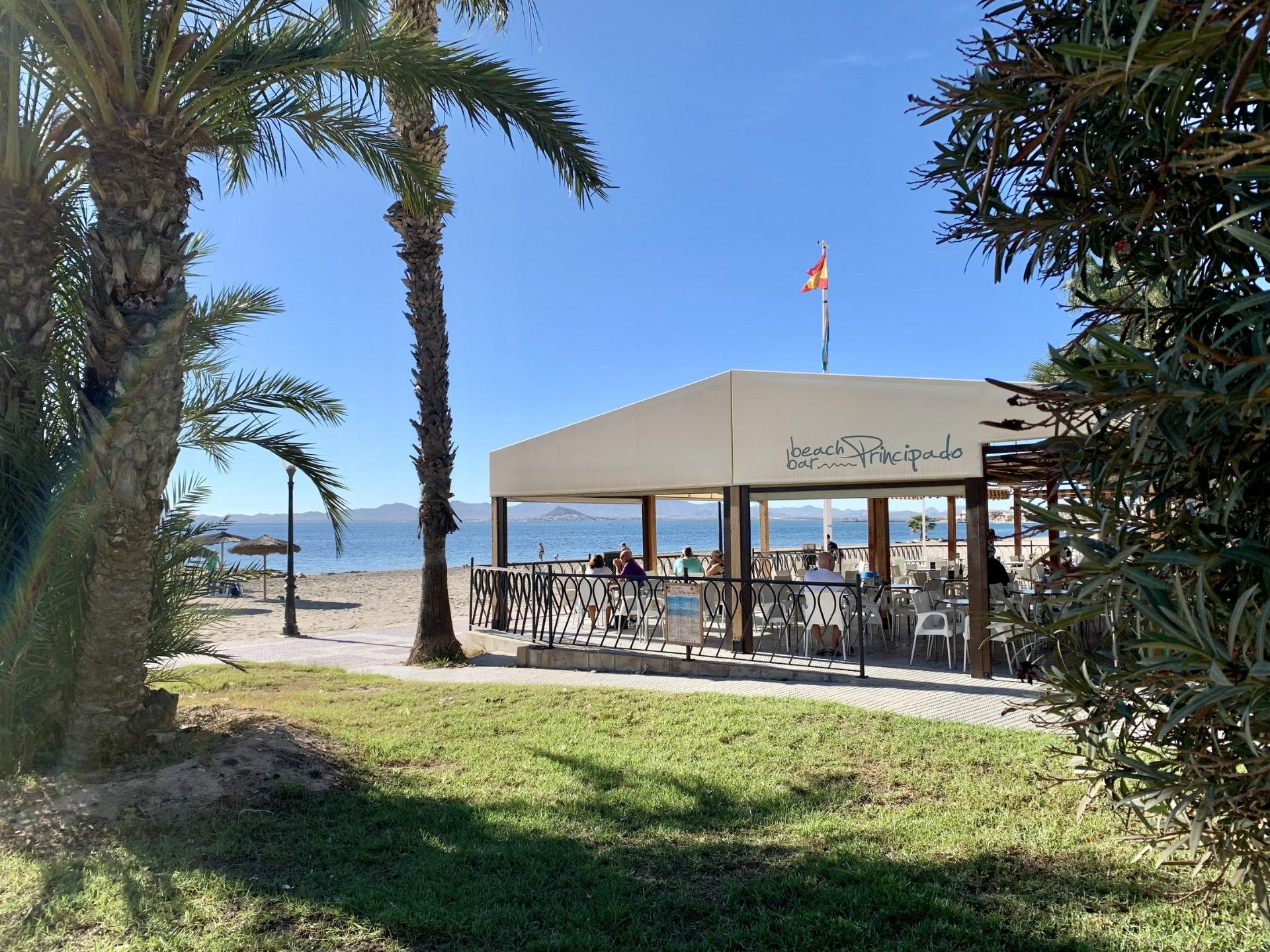 Sunlit beachfront terrace with palm trees overlooking the pristine beach near luxury new build villas in Los Alcázares, Murcia.