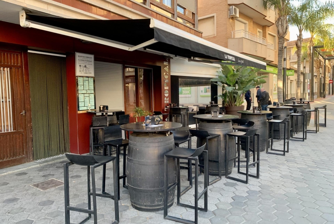 Trendy outdoor dining area with modern barrel tables and stools on sunlit street near luxury villas in Los Alcázares, Murcia