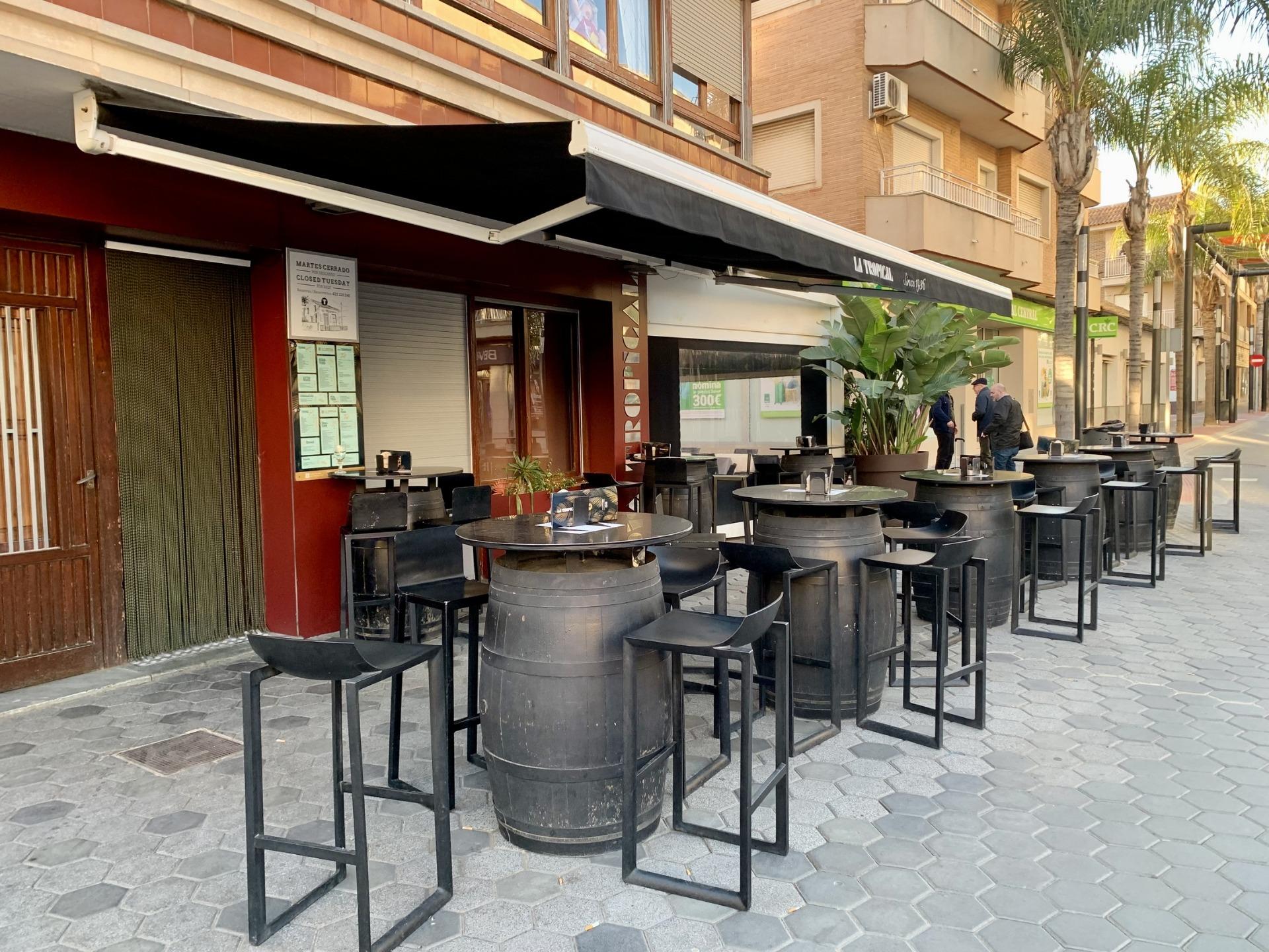 Trendy outdoor dining area with modern barrel tables and stools on sunlit street near luxury villas in Los Alcázares, Murcia