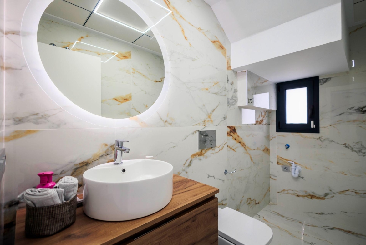 Elegant modern bathroom with marble walls and backlit mirror in new build villas on Pilar de la Horadada golf course