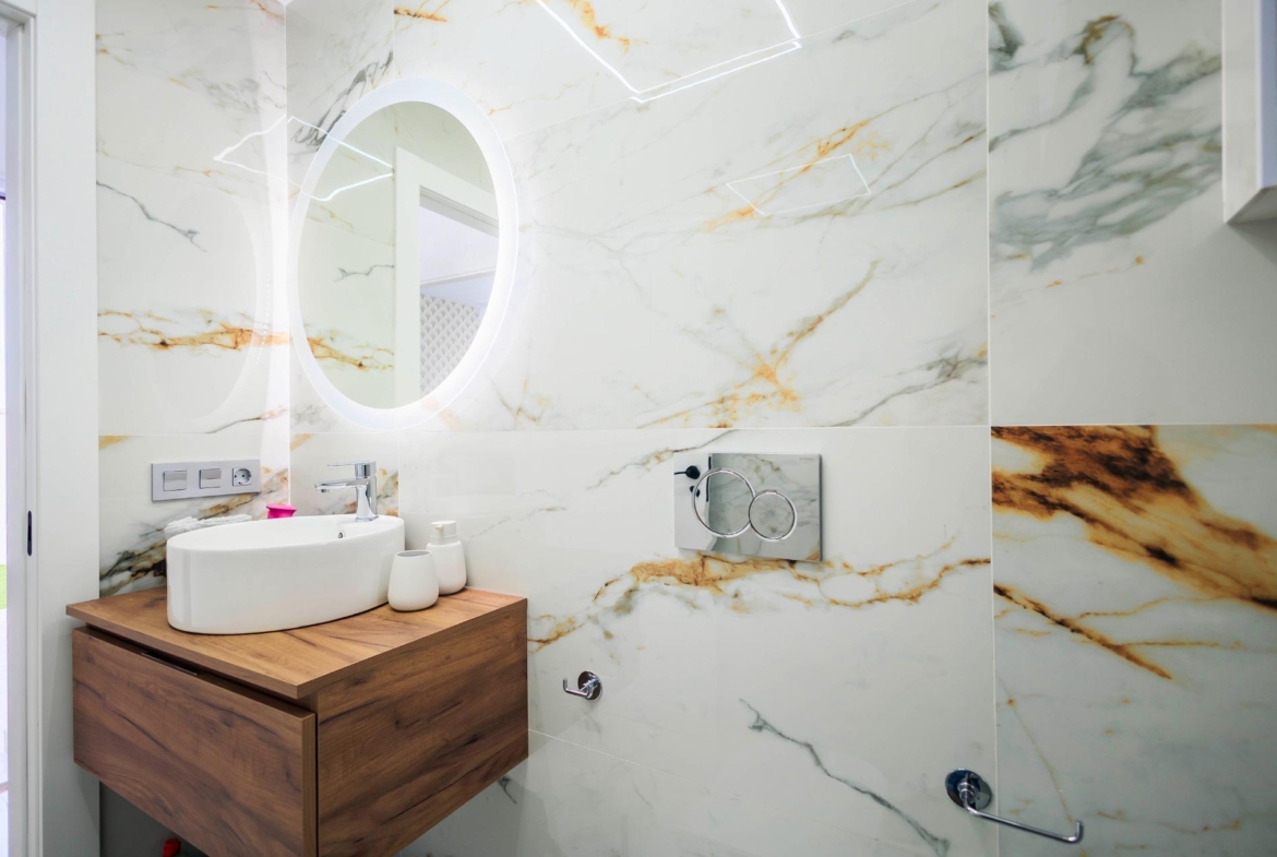 Elegant marble-clad bathroom with illuminated mirror and modern wooden vanity in new build villas in Pilar de la Horadada on the golf course