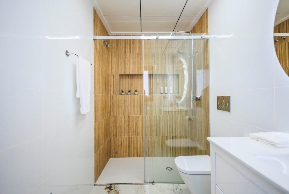 Bright modern bathroom with sleek glass shower and warm wood paneling in new build villas at Pilar de la Horadada golf course.