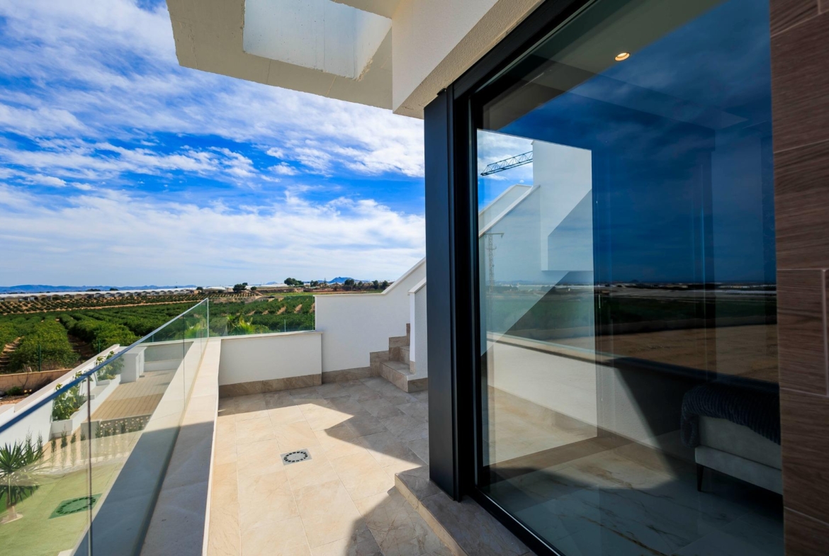 NEW-BUILD-VILLAS-IN-PILAR-DE-LA-HORADADA-ON-THE-GOLF-COURSE-32 Sun-drenched terrace with glass railing overlooking landscaped golf course in modern new build villas in Pilar de la Horadada