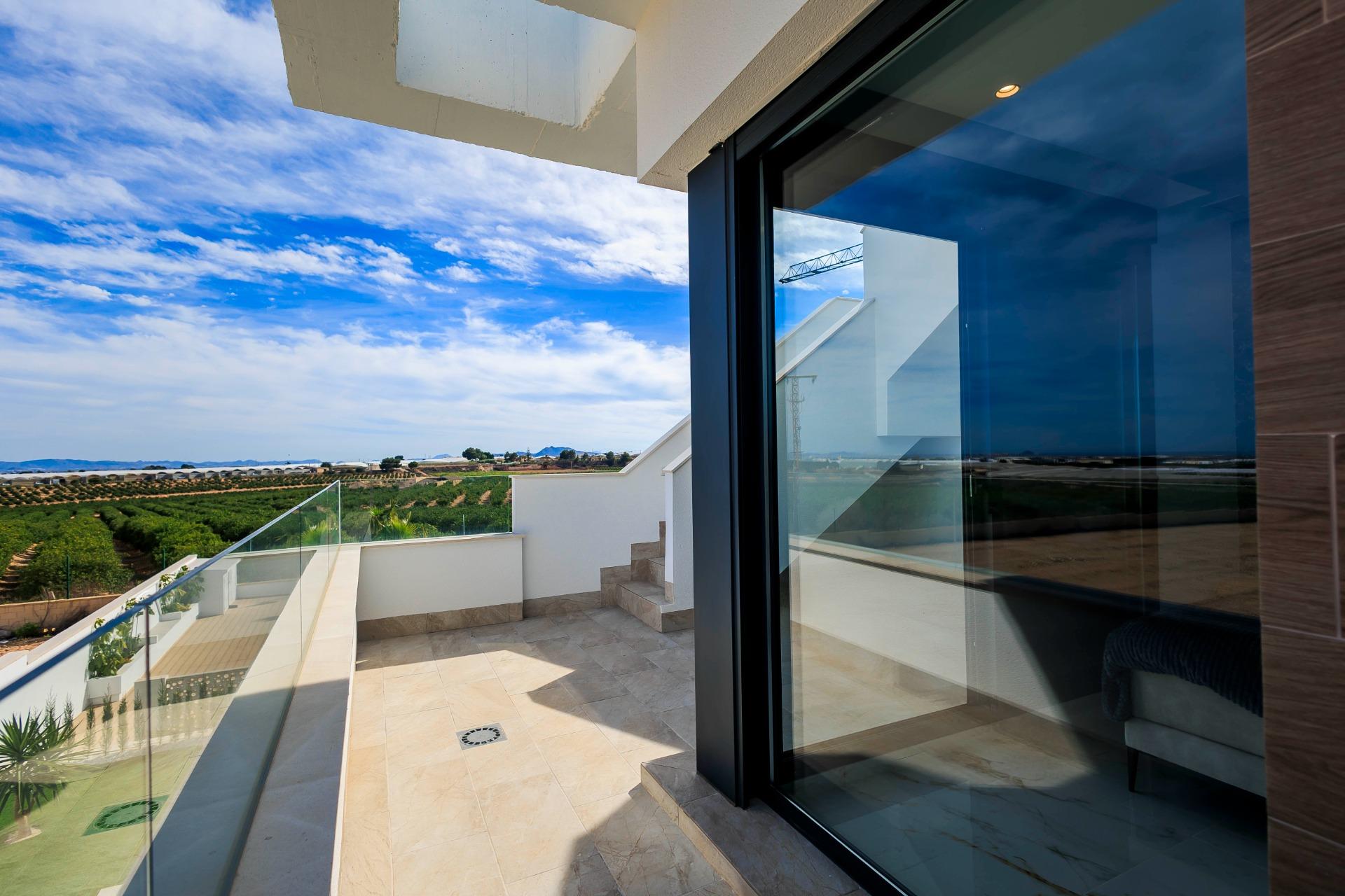 Bright sun-drenched terrace with glass railing and panoramic golf course views at new build villas in Pilar de la Horadada.
