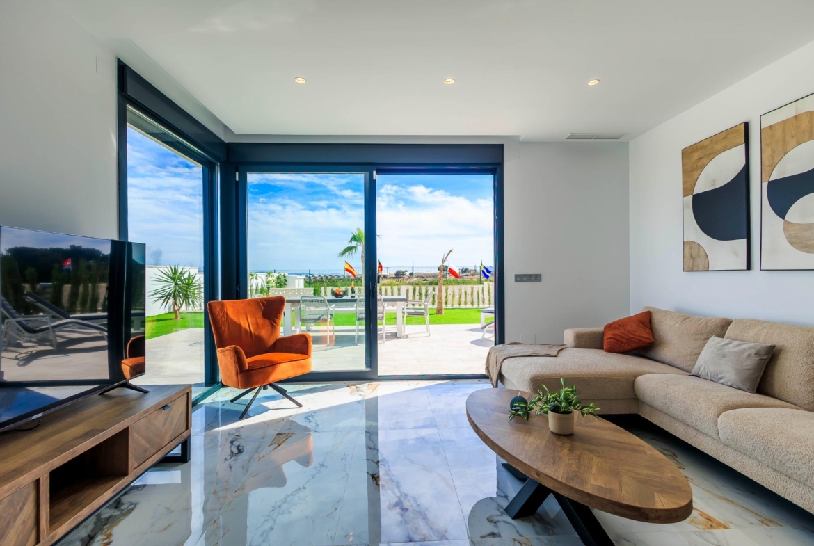 Bright modern living room with marble floors and sliding glass doors opening to a sunlit terrace in new Pilar de la Horadada villas.