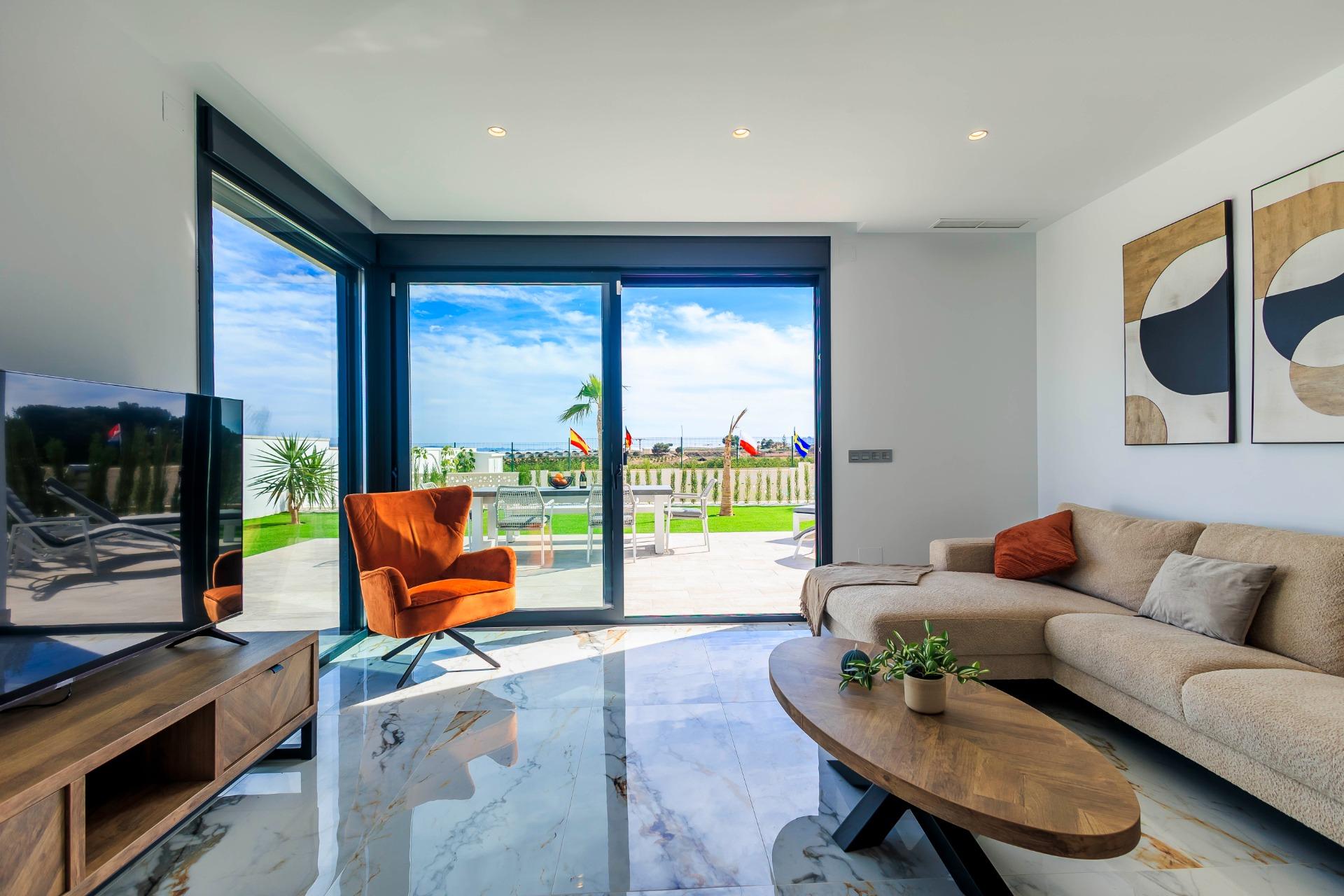 Bright modern living room with marble floors and sliding glass doors opening to a sunlit terrace in new Pilar de la Horadada villas.
