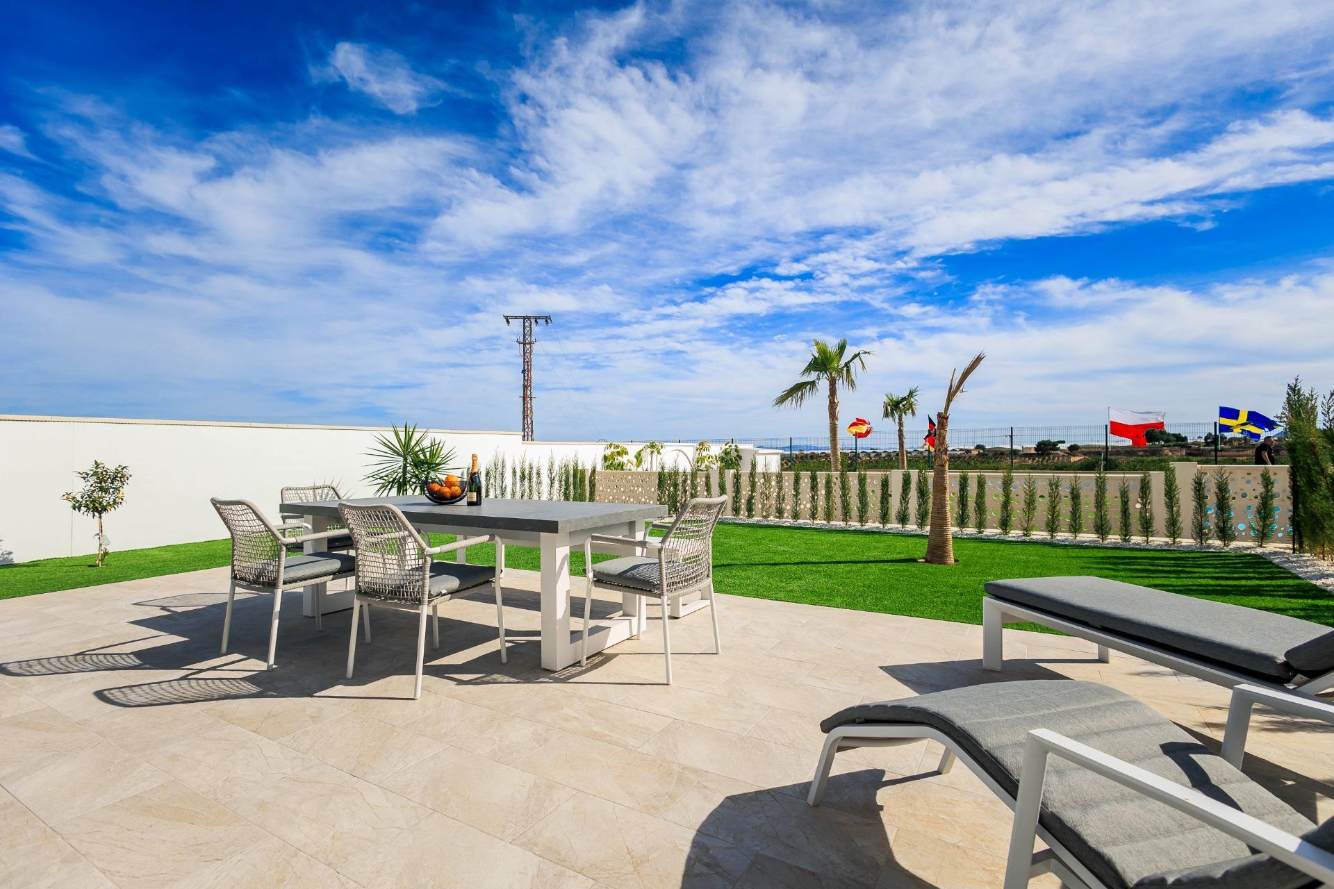Sun-drenched modern terrace with elegant outdoor dining and loungers at new build villas in Pilar de la Horadada golf course