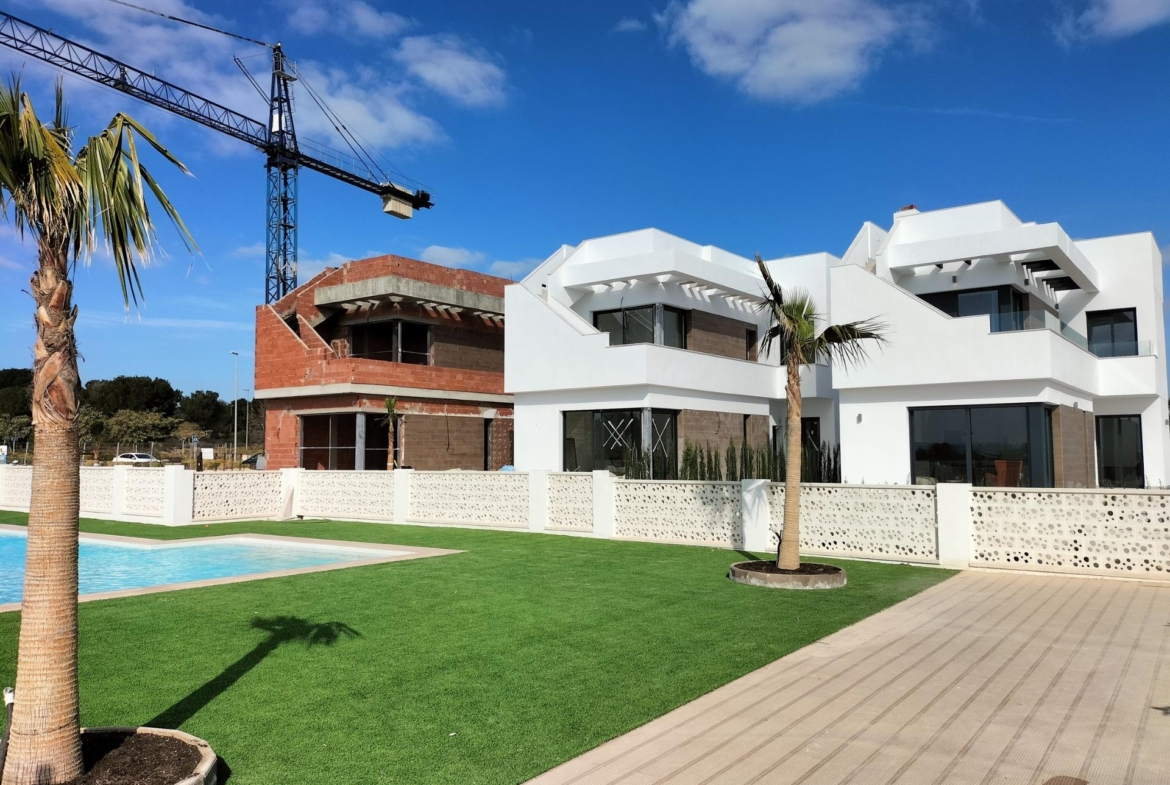 NEW BUILD VILLAS IN PILAR DE LA HORADADA ON THE GOLF COURSE Modern new build villas in Pilar de la Horadada with spacious terraces, lush green lawn, pool, and golf course views under a bright blue sky.