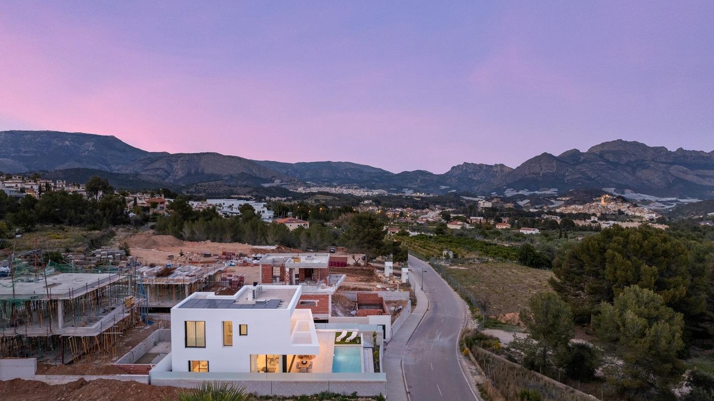 Modern white 3-bedroom villa with private pool, nestled in landscaped surroundings by serene road in Polop, Costa Blanca at sunset.