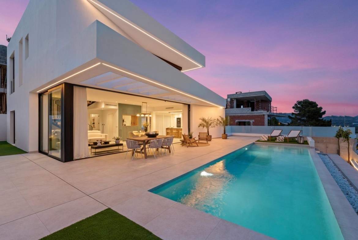 Modern 3-bedroom villa in Polop with expansive terrace, sleek open-plan interior, and illuminated private pool at sunset.