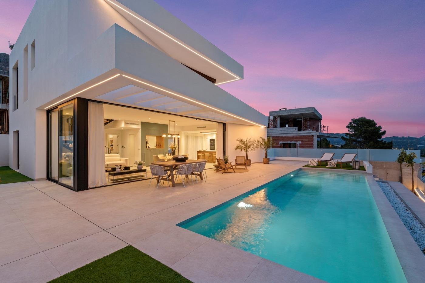 Modern 3-bedroom villa in Polop with expansive terrace, sleek open-plan interior, and illuminated private pool at sunset.