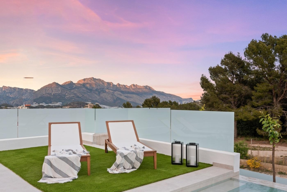 Sunset terrace with modern lounge chairs, sleek glass fence, and panoramic mountain views at luxury 3-bedroom villa in Polop, Costa Blanca