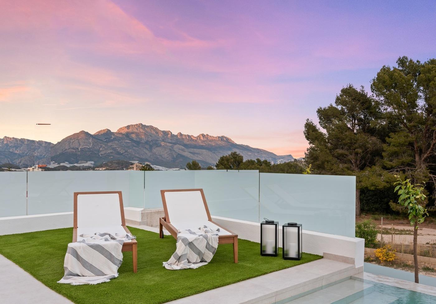 Sunset terrace with modern lounge chairs, sleek glass fence, and panoramic mountain views at luxury 3-bedroom villa in Polop, Costa Blanca