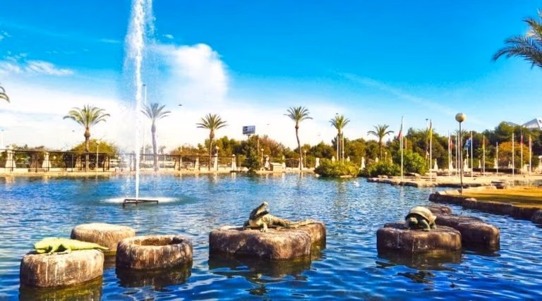 NEW-BUILD-VILLAS-IN-TORREVIEJA-18 Serene water feature with stone sculptures and palm trees under a bright sky, reflecting the tranquil lifestyle of Aguas Nuevas, Torrevieja.