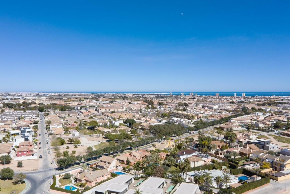 Modern new built villa on a floor with private landscaped gardens, surrounded by a sunlit residential area and distant sea views.