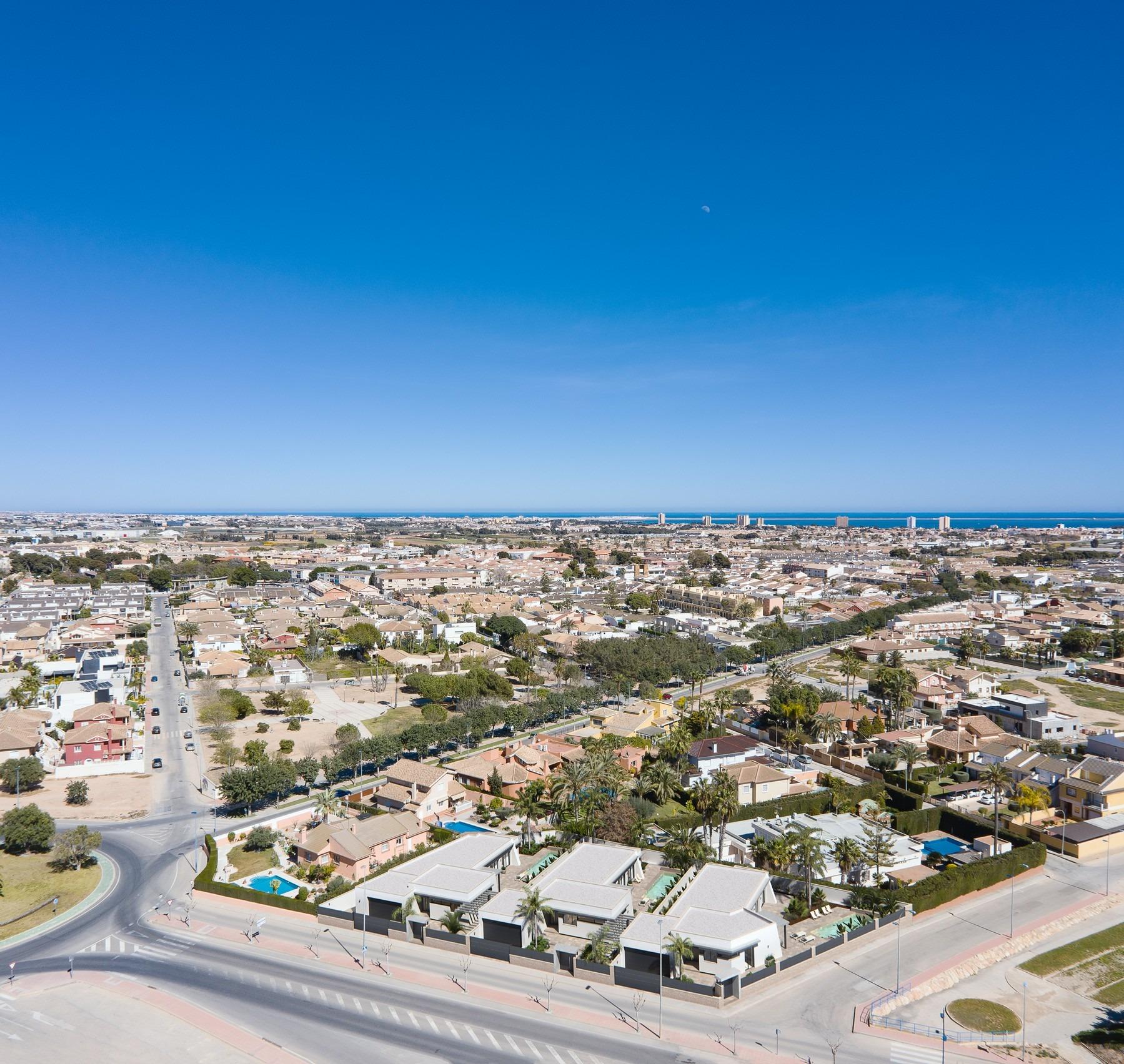 Modern new built villa on a floor with private landscaped gardens, surrounded by a sunlit residential area and distant sea views.