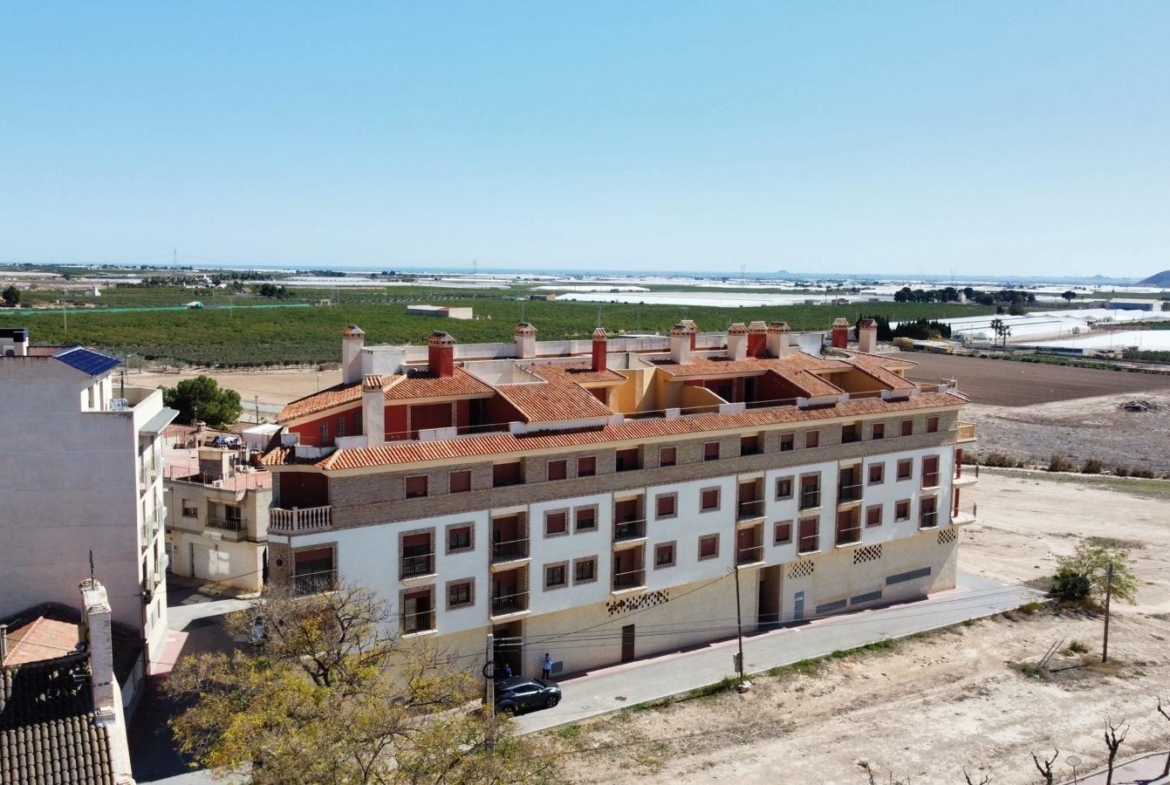 Bright, modern studio apartment building in sunny Avileses, Murcia, surrounded by open countryside and distant sea views.