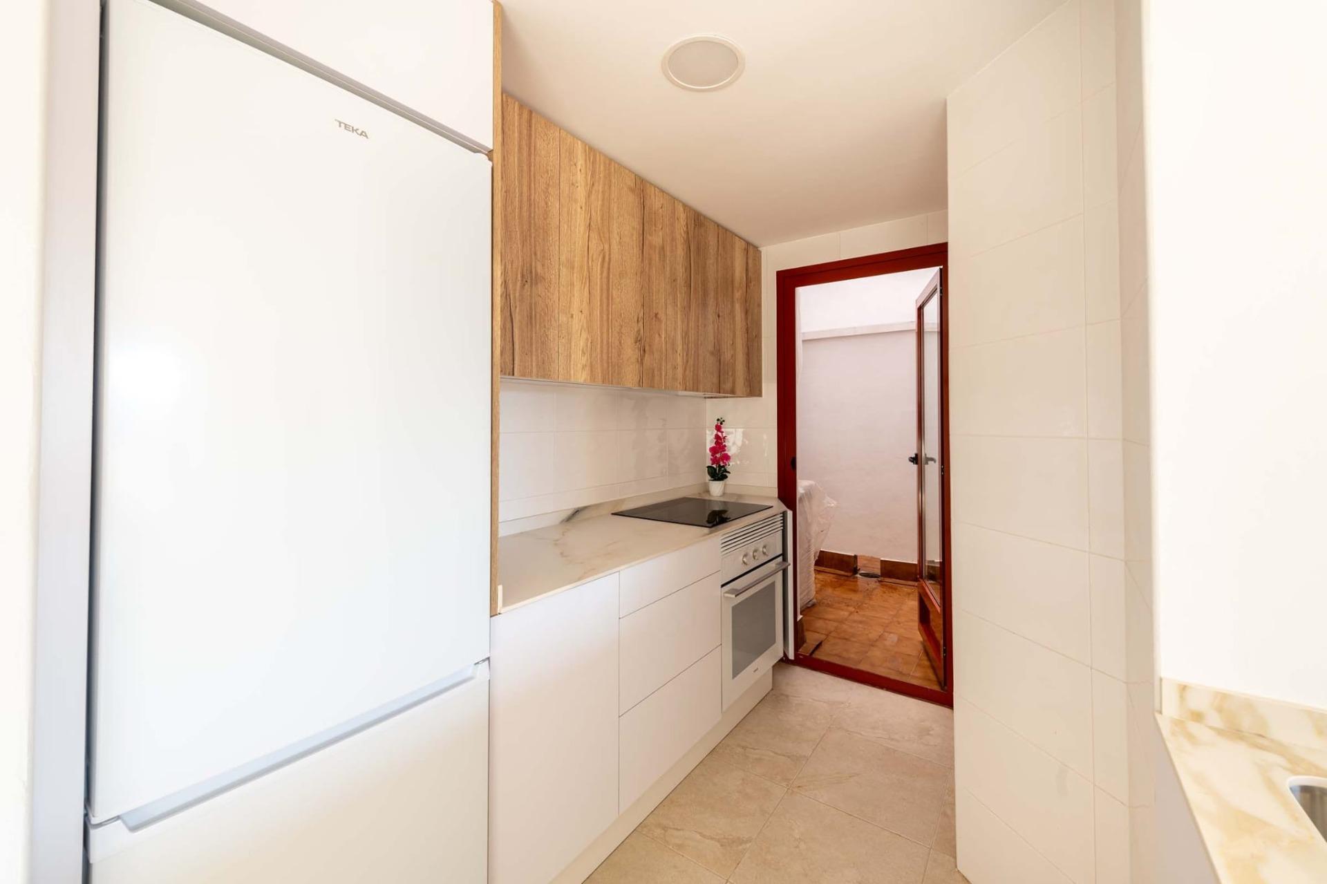 Bright modern kitchen with sleek white cabinets and wood accents in a new 1-bedroom apartment in Avileses, Murcia.