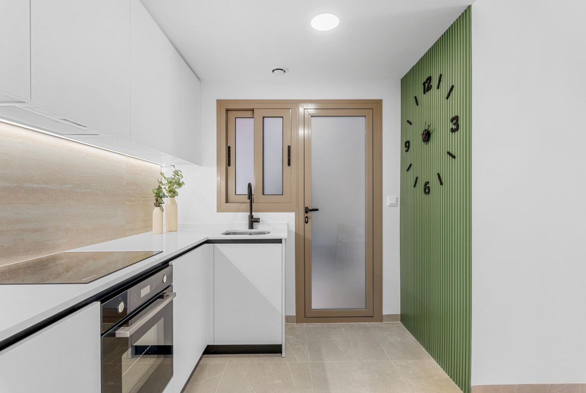 Bright modern kitchen with sleek white cabinetry and green accent wall in 3-bedroom penthouse for sale in Jacarilla.