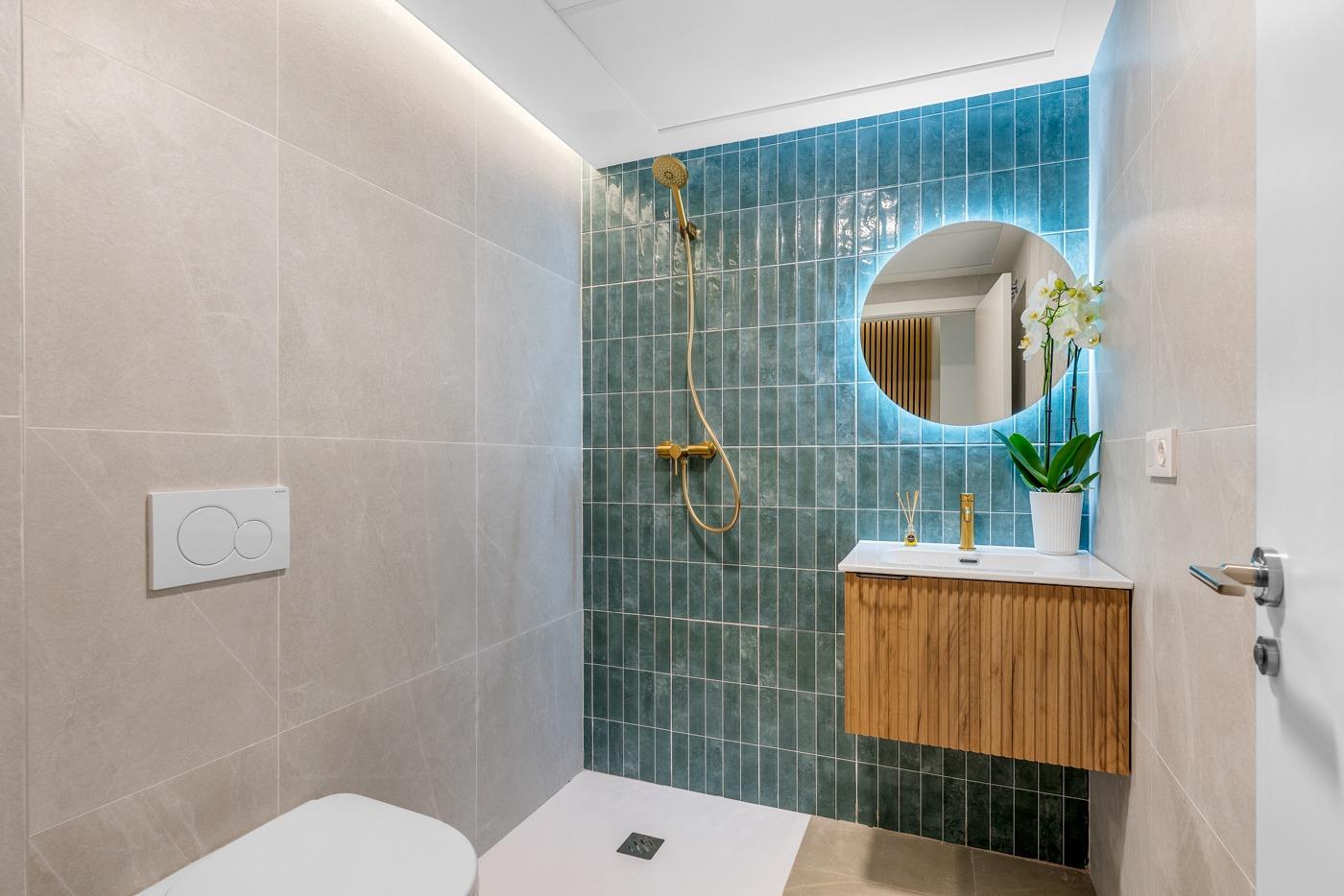 Modern bathroom with elegant gold fixtures and vibrant teal tile wall in a new build 3-bedroom ground floor apartment in Jacarilla
