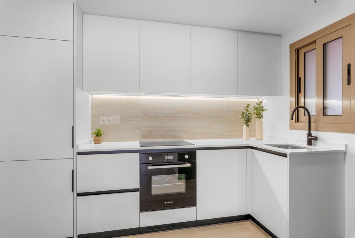 Modern, sleek kitchen with white cabinetry and stone backsplash in luxury 3-bedroom penthouse in Jacarilla.