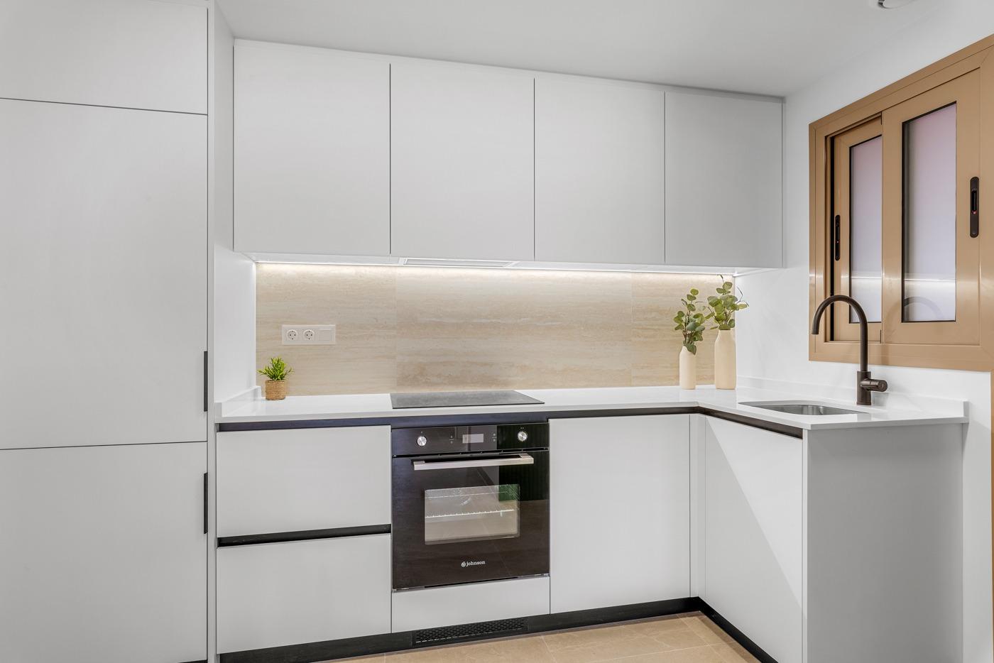 Modern, sleek kitchen with white cabinetry and stone backsplash in luxury 3-bedroom penthouse in Jacarilla.