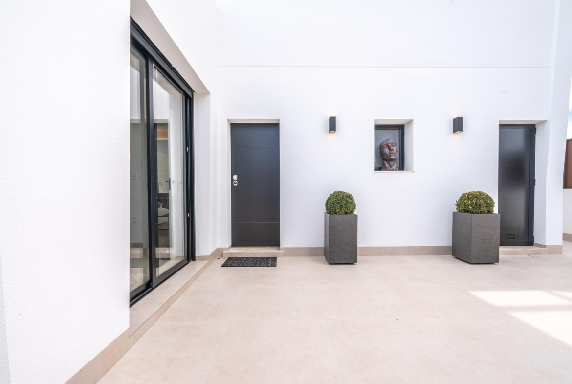 Spacious sunlit courtyard with sleek black doors and minimalist planters in Mediterranean single-storey villa, Roldán Torre-Pacheco.