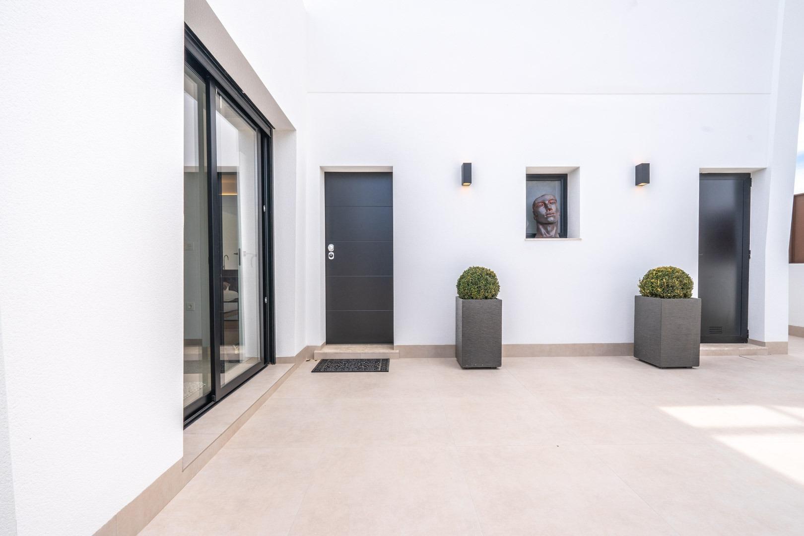 Spacious sunlit courtyard with sleek black doors and minimalist planters in Mediterranean single-storey villa, Roldán Torre-Pacheco.