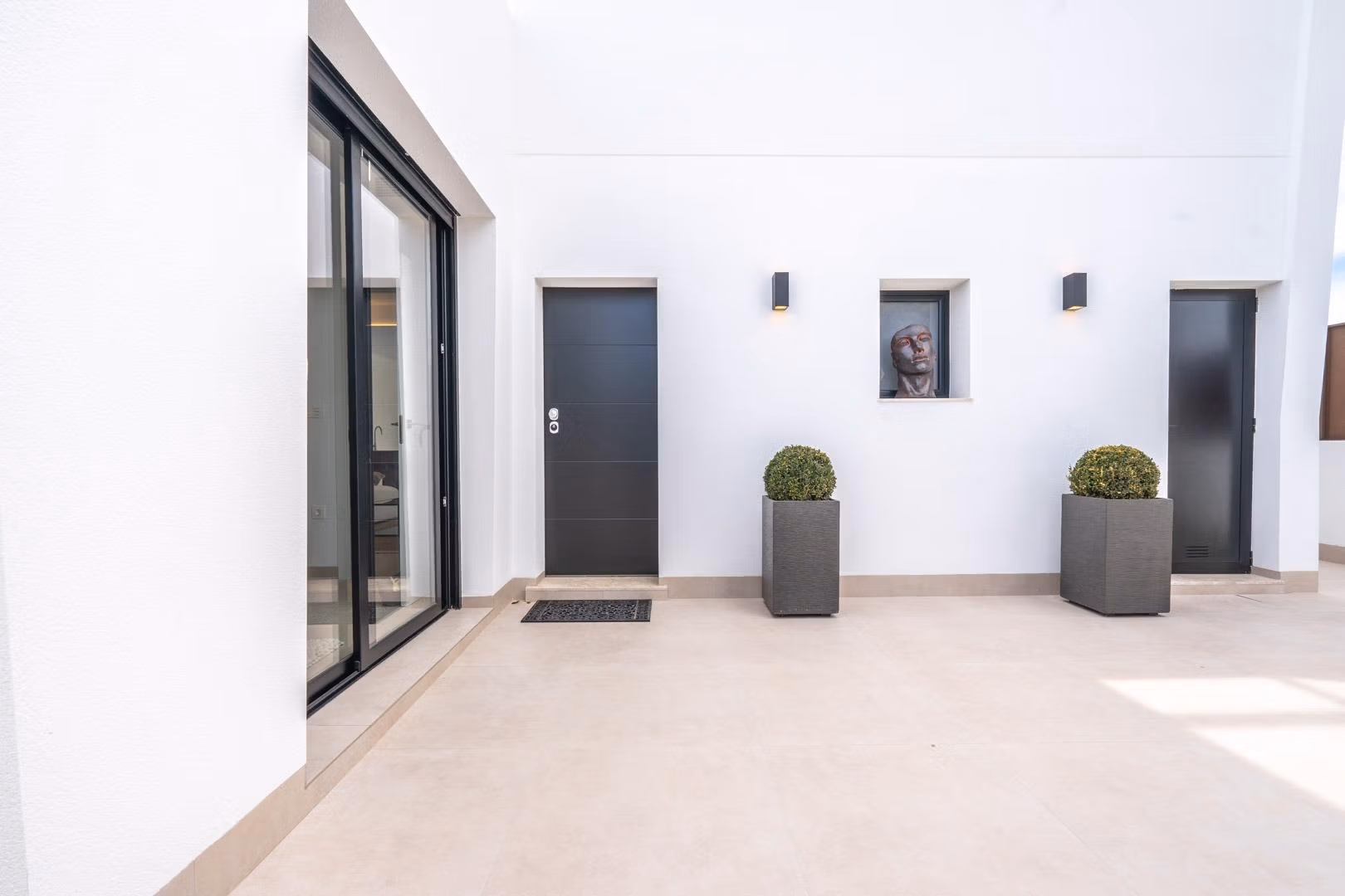 Spacious sunlit courtyard with sleek black doors and minimalist planters in Mediterranean single-storey villa, Roldán Torre-Pacheco.