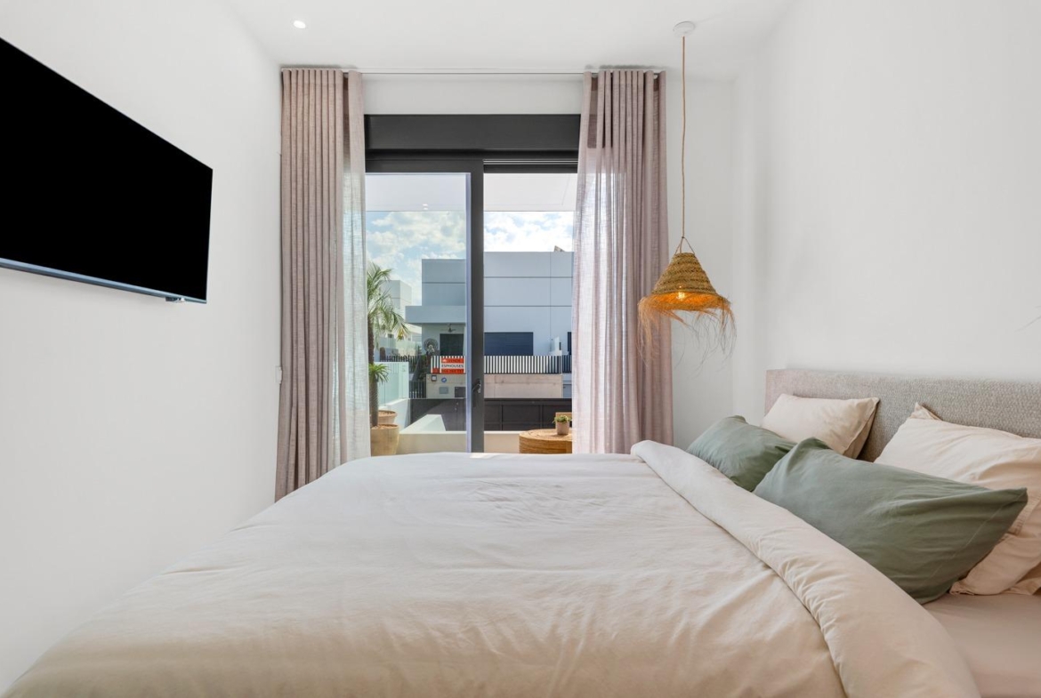 Bright modern bedroom with soft linens and sliding glass doors opening to a balcony in a new 3-bedroom villa in Dolores, Alicante.