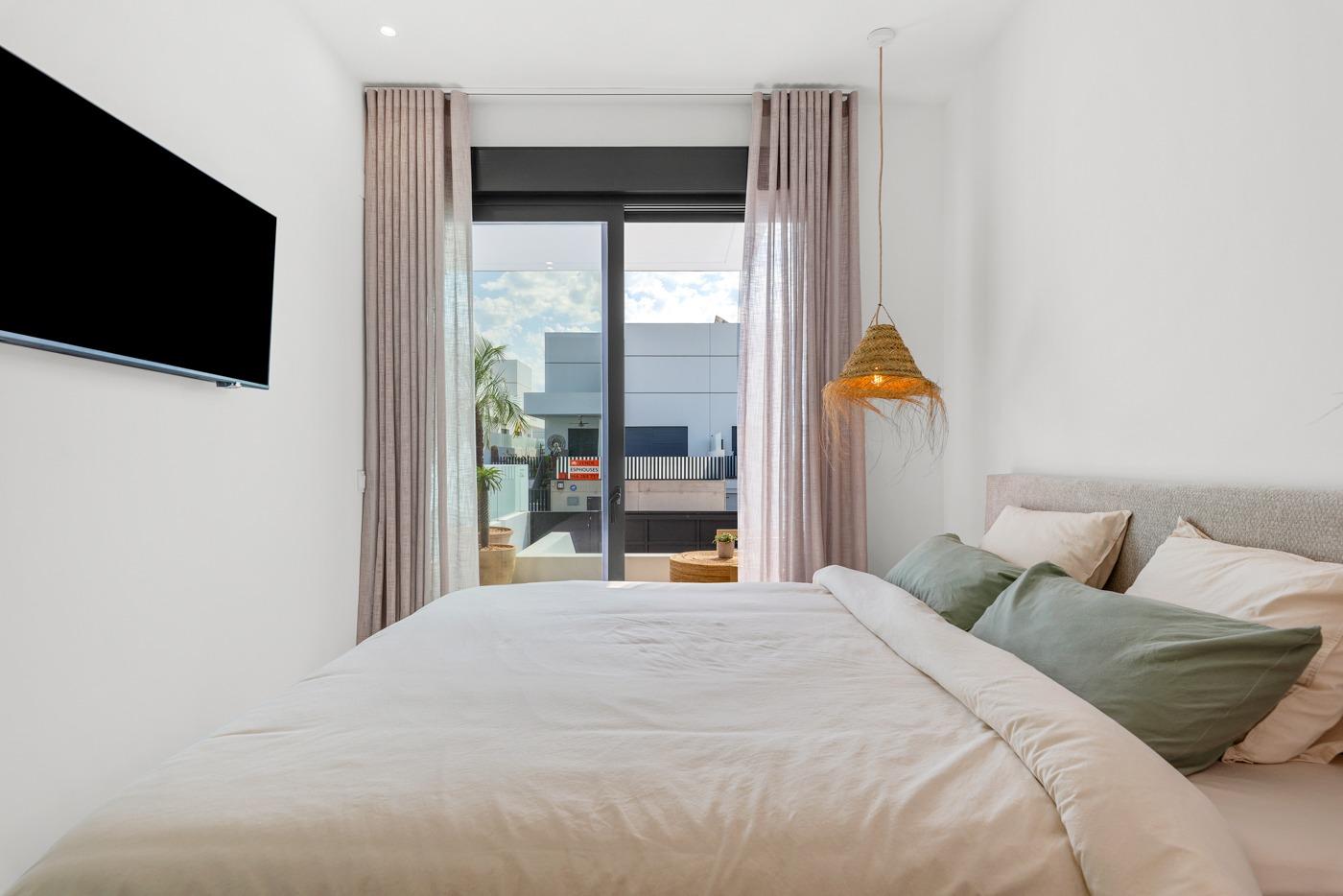 Bright modern bedroom with soft linens and sliding glass doors opening to a balcony in a new 3-bedroom villa in Dolores, Alicante.
