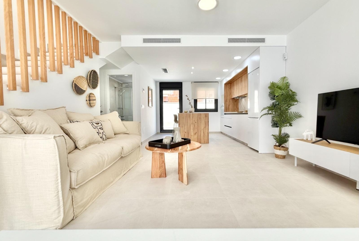 Bright, modern living room and open-plan kitchen in a new 2-bedroom townhouse in Cox, Alicante with elegant wood accents.