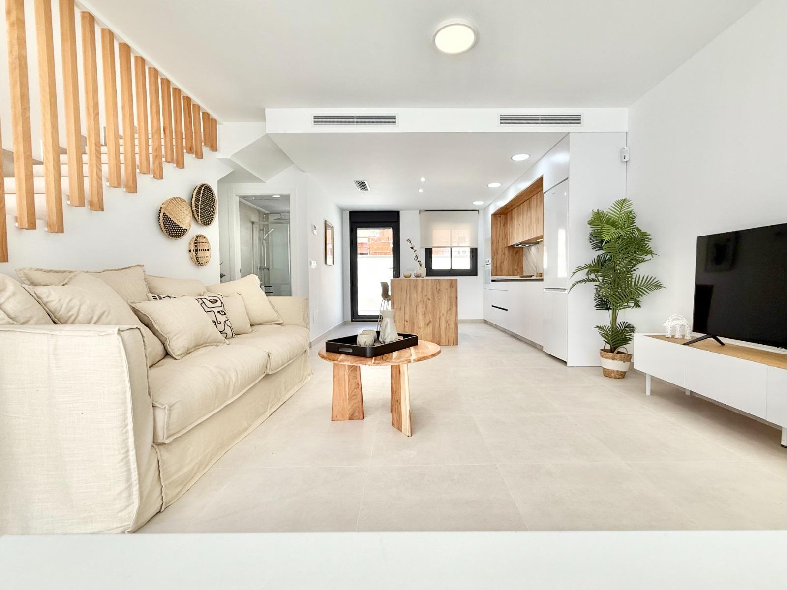 Bright, modern living room and open-plan kitchen in a new 2-bedroom townhouse in Cox, Alicante with elegant wood accents.
