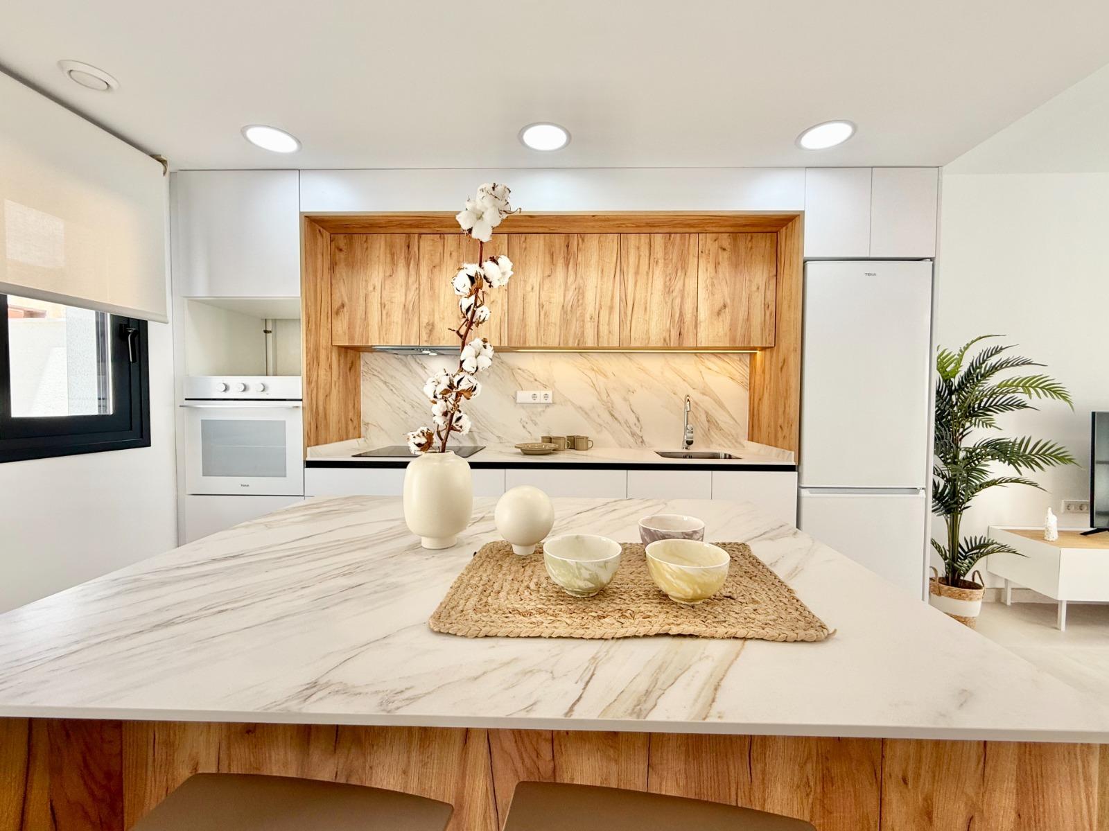 Bright modern kitchen with sleek marble countertops and wood accents in new 2-bedroom townhouse in Cox, Alicante.