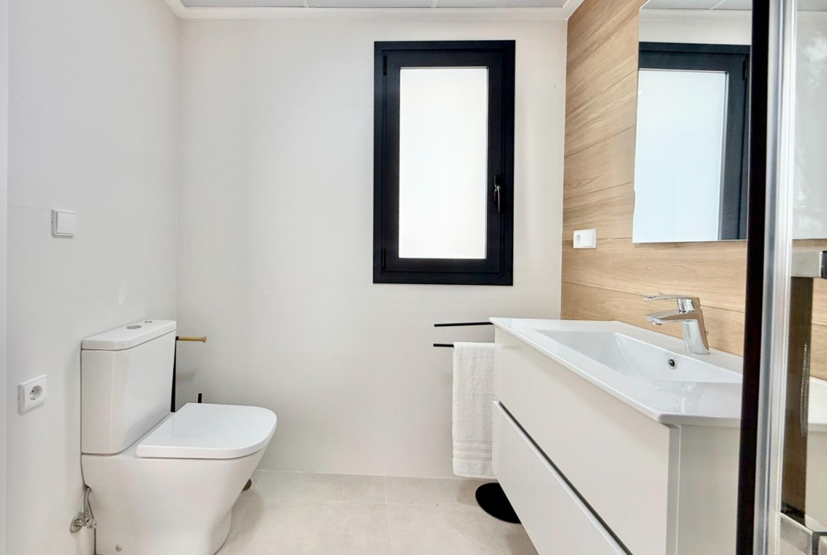 Bright, modern bathroom with sleek fixtures and wood-accented wall in affordable 2-bedroom townhouse in Cox, Alicante.
