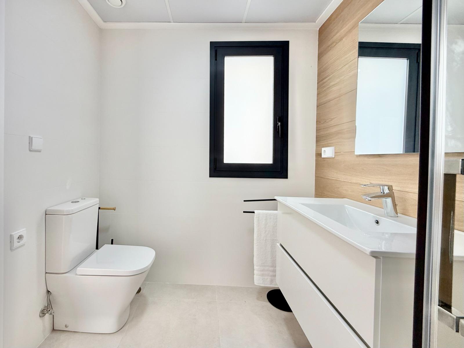 Bright, modern bathroom with sleek fixtures and wood-accented wall in affordable 2-bedroom townhouse in Cox, Alicante.