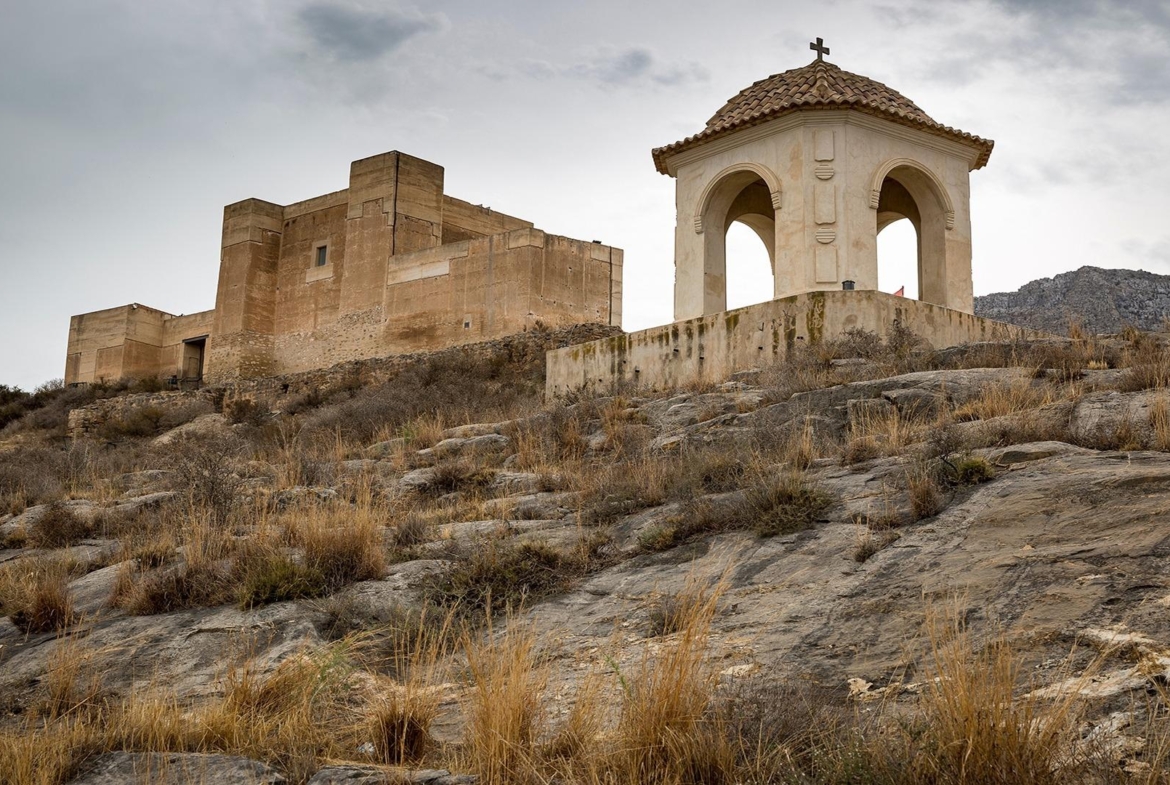 Historic stone chapel and fortress set on rugged hillside near Cox, Alicante, offering unique panoramic views and serene surroundings.