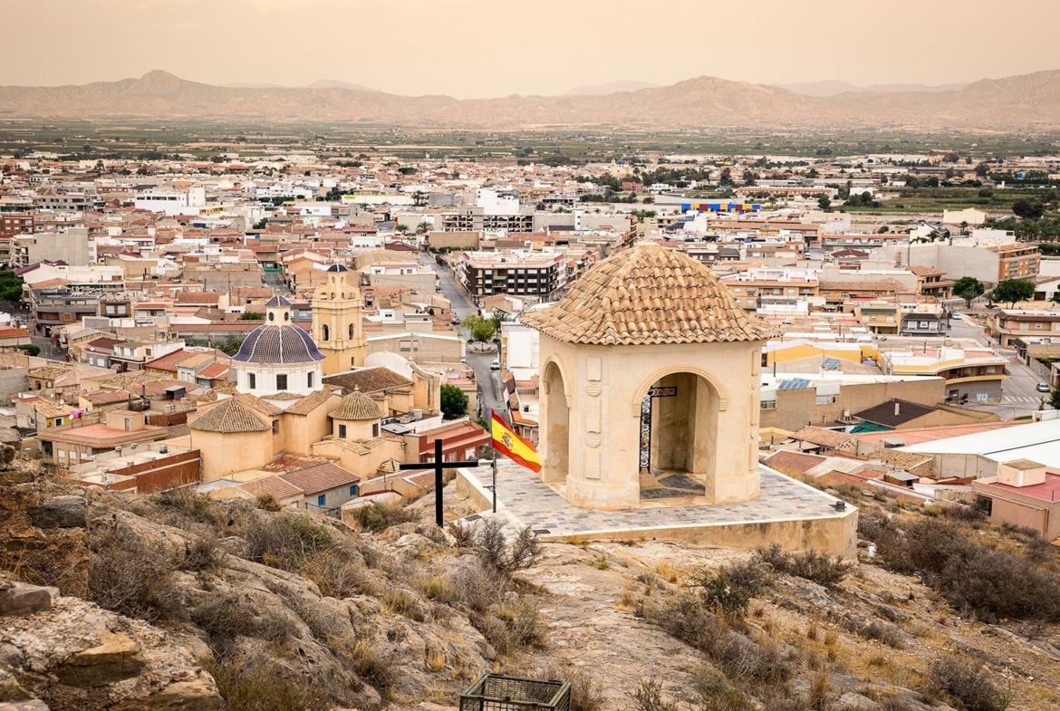 Panoramic view over historic Cox, Alicante with traditional rooftops and distant mountains under a soft, warm sky