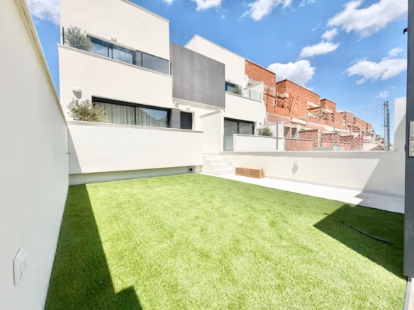 Helle moderne Außenansicht eines Reihenhauses mit privater sonniger Terrasse und üppiger Rasenfläche in Cox, Alicante.