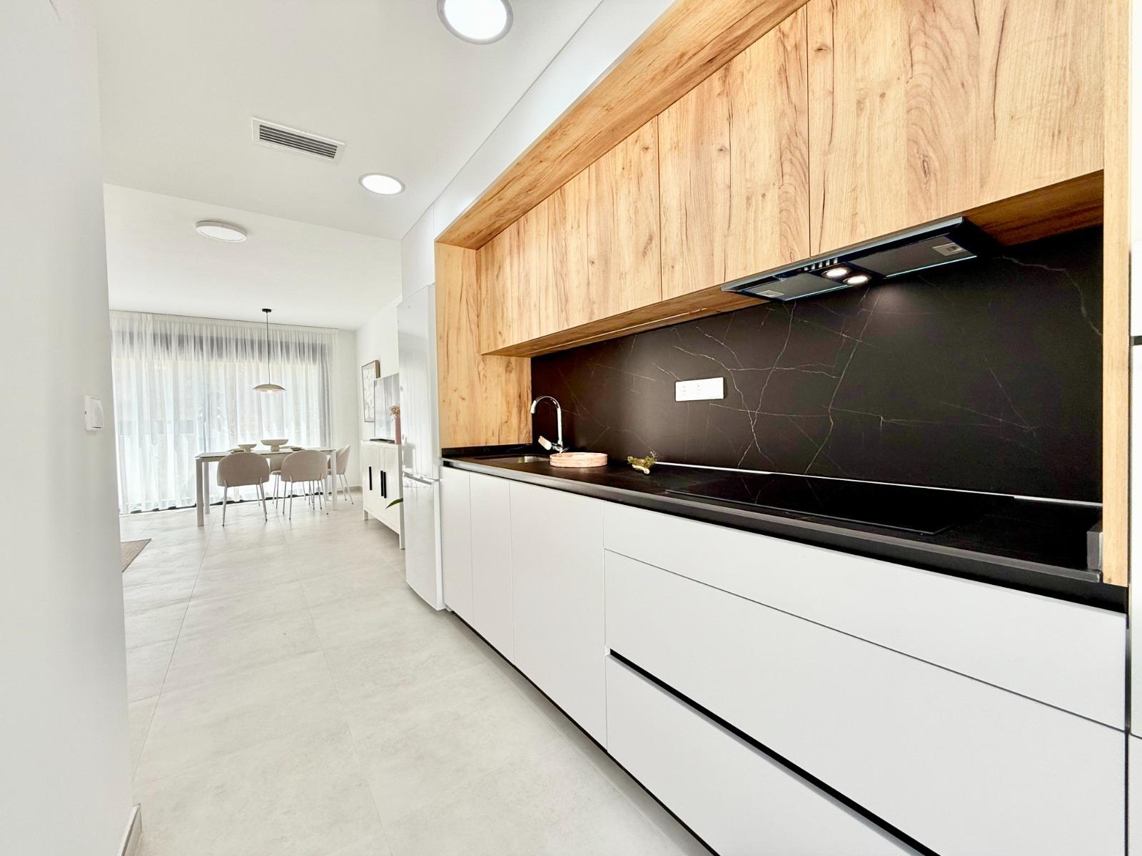 Bright modern kitchen with sleek black countertop and wood cabinets in spacious 3 bedroom townhouse in Cox, Alicante.