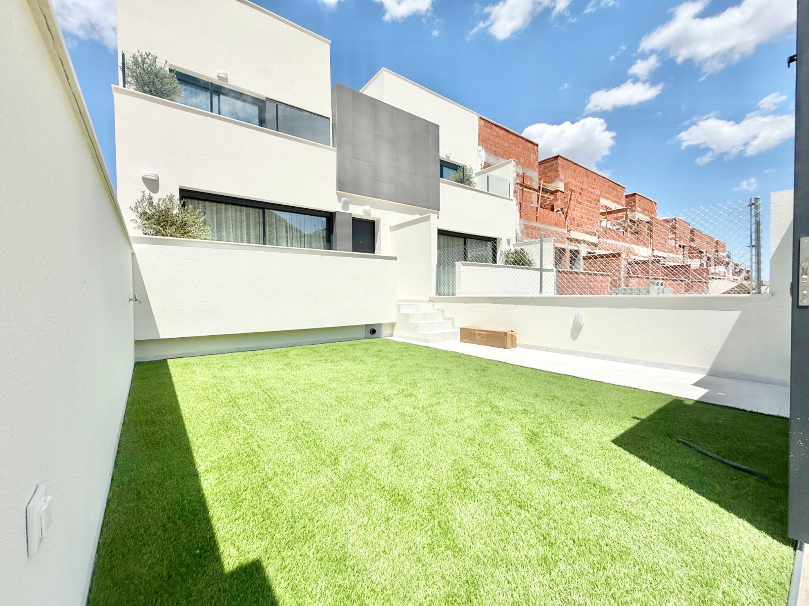 Bright modern townhouse exterior with private sun-drenched terrace and lush lawn in Cox, Alicante.