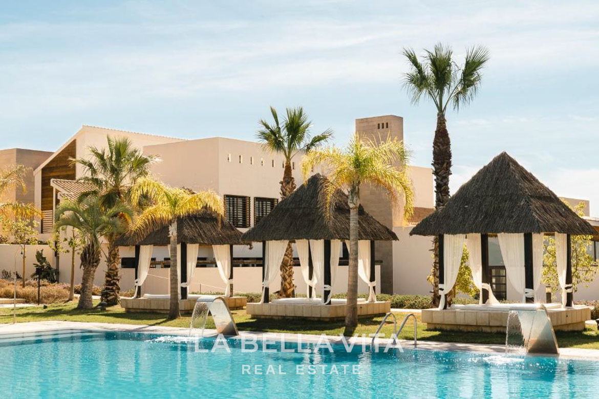 Sun-drenched pool area with elegant shaded cabanas and palm trees at single-storey new build villa in Hacienda del Álamo Golf Resort Murcia